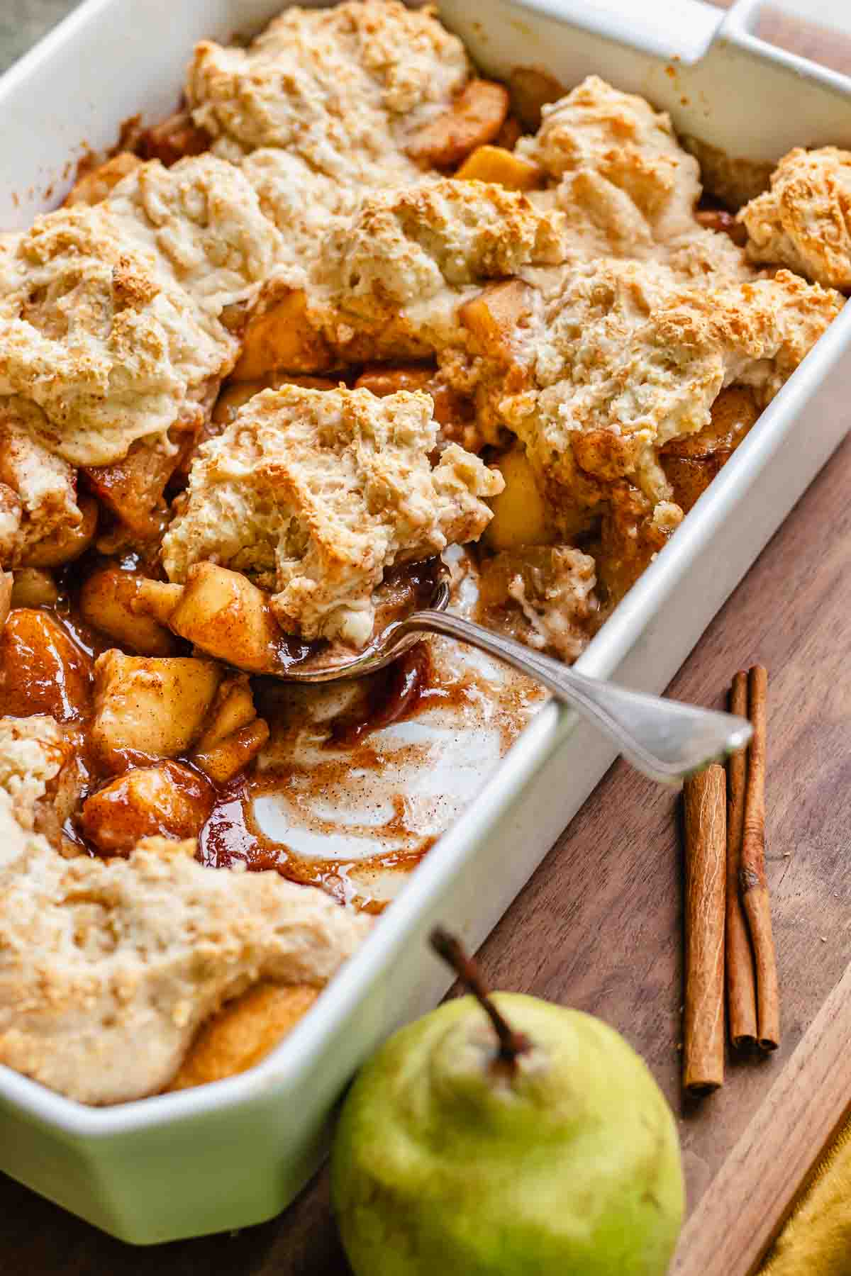 A spoon sits in a casserole dish with a scoop of pear cobbler in it.