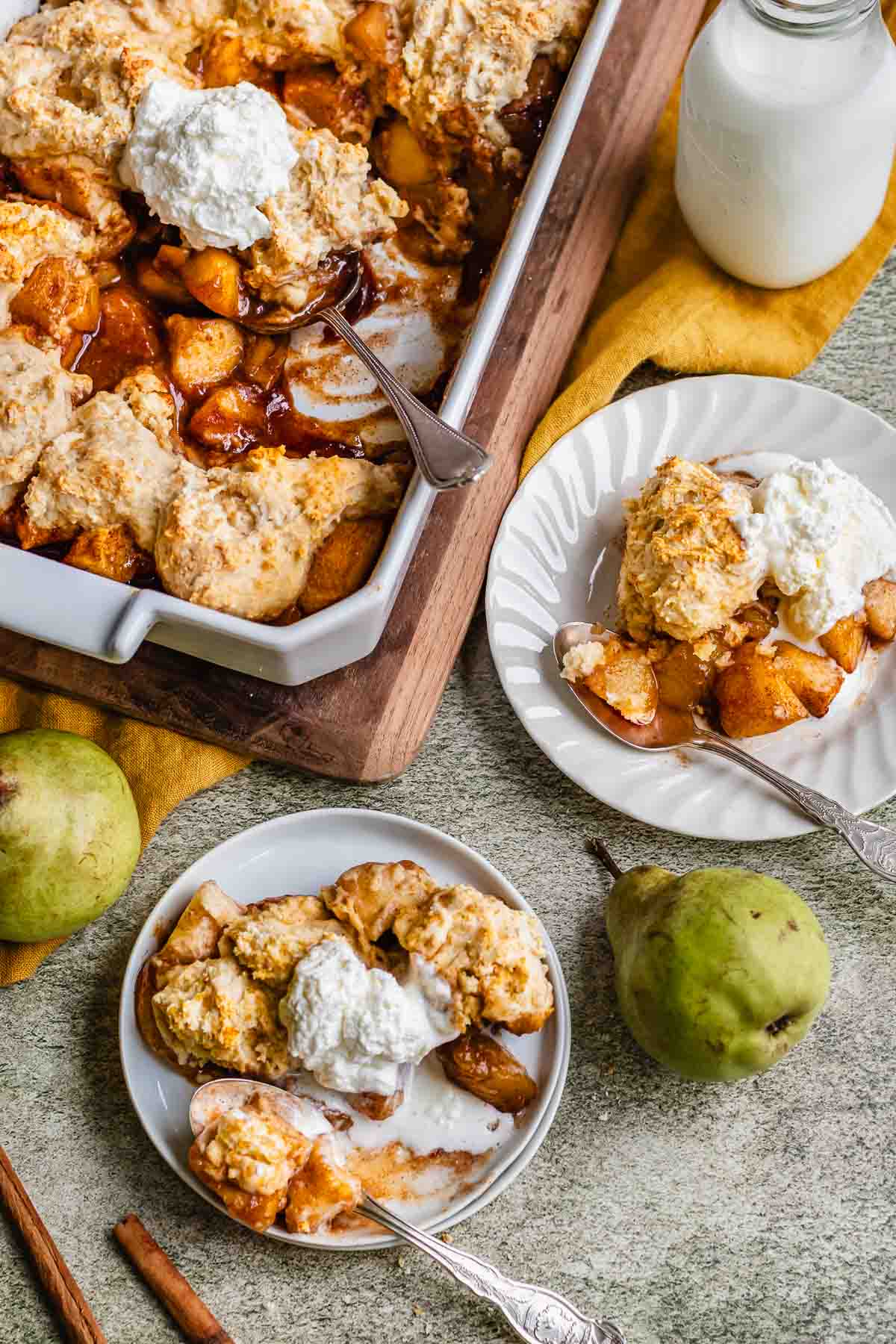 Two plates of pear cobbler next to a casserole dish.