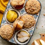 Baked pear muffins in a muffin tin. One sits in the middle with a bite removed.