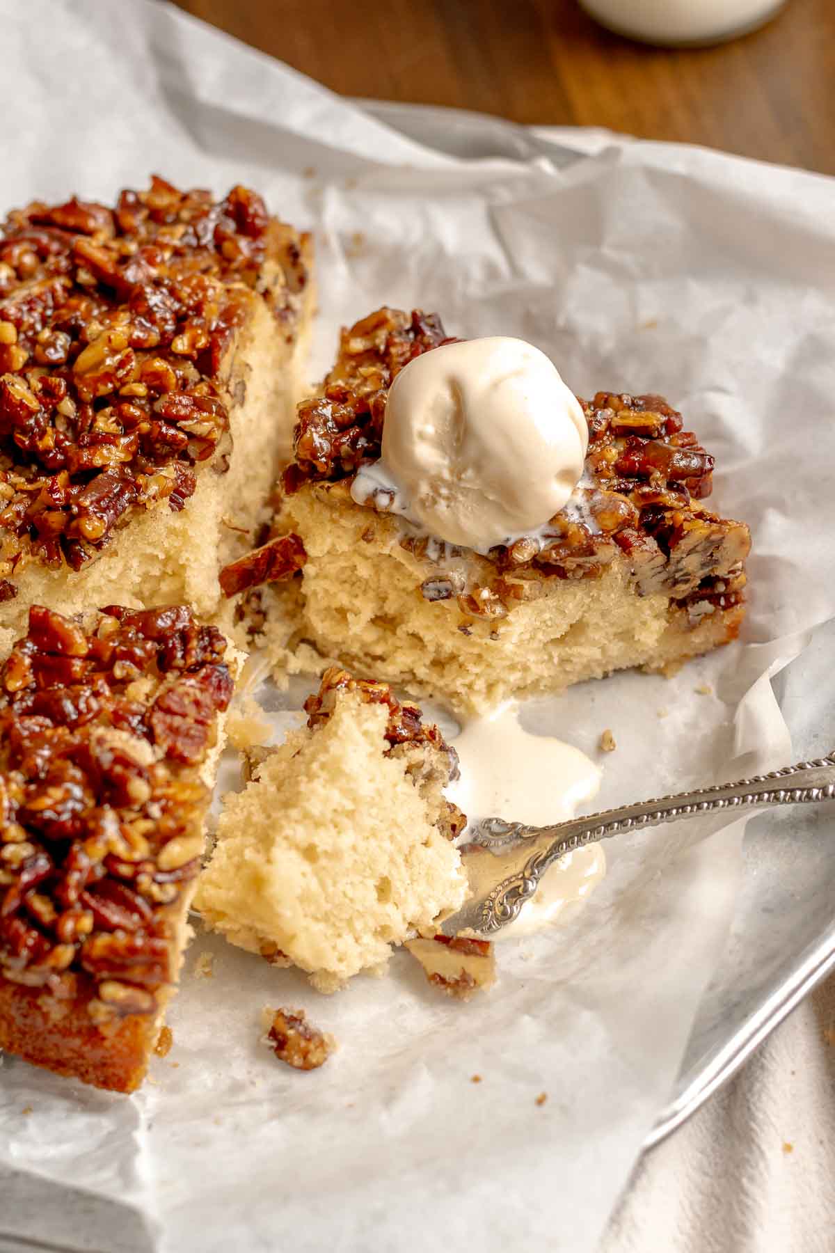 A fork removes a bite of upside down pecan cake on a platter with melted ice cream on top.