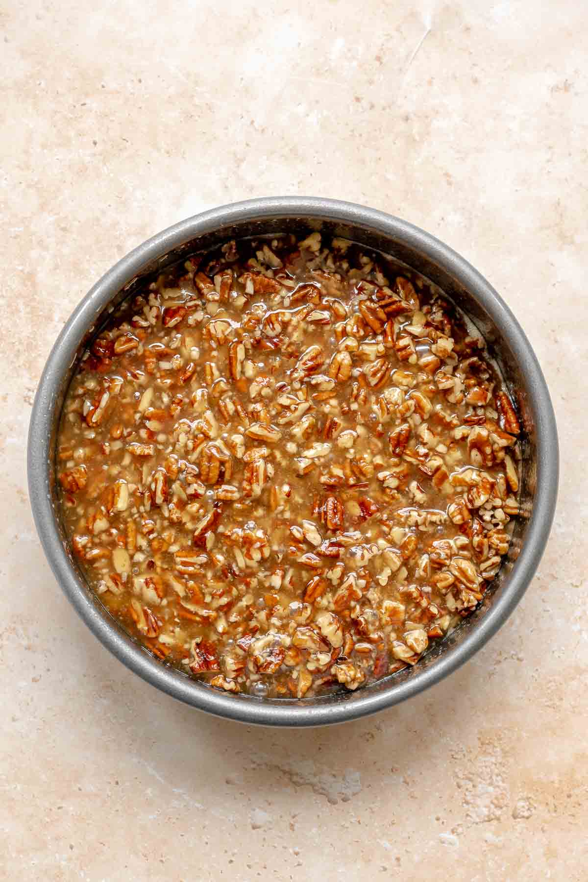 Pecans and syrup spread into the bottom of a cake pan.