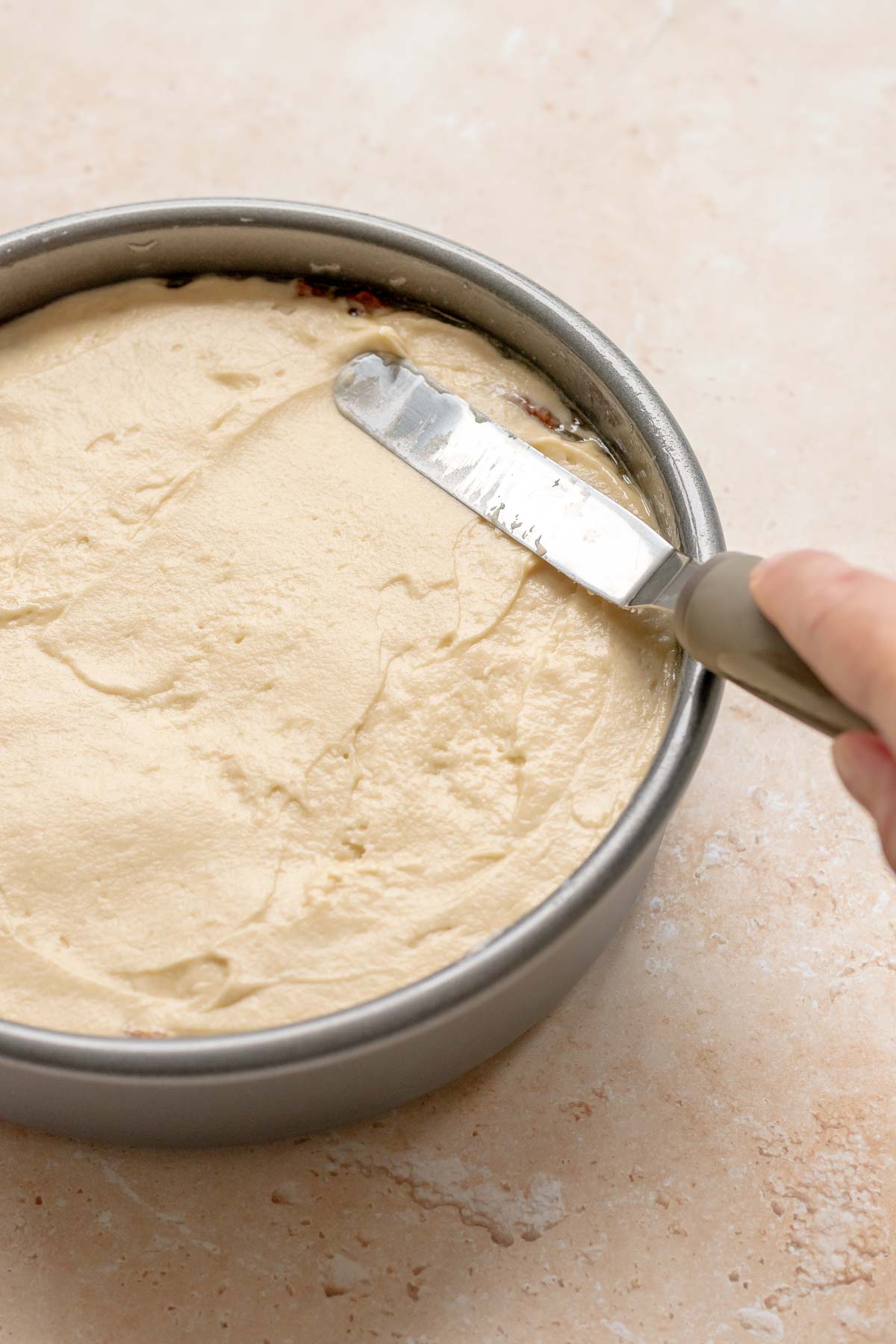 An offset spatula spreads cake batter to the edges of a pan.
