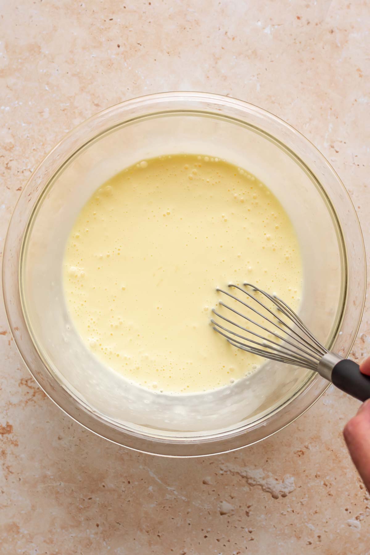 A hand whisks eggs and cream in a bowl.