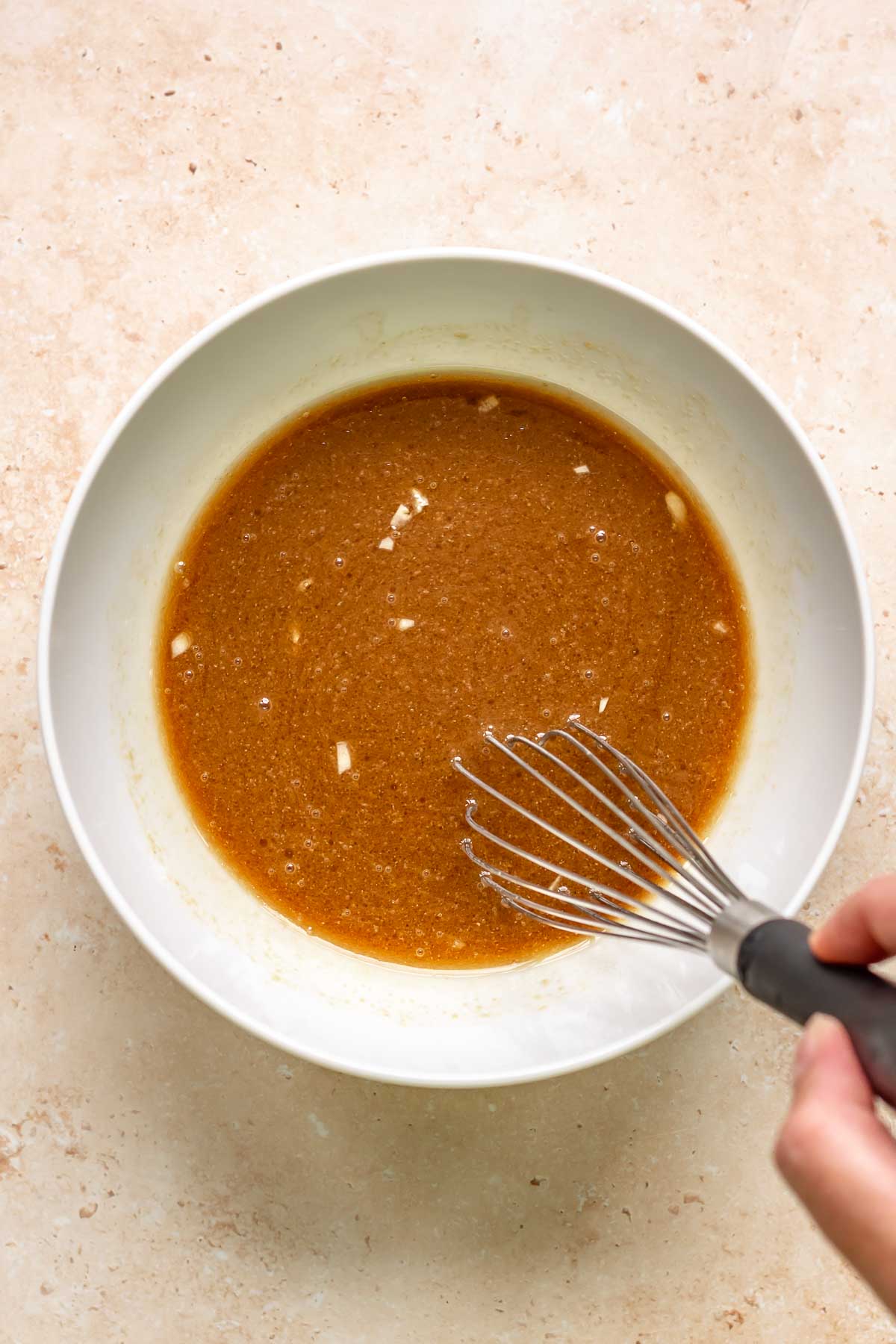 A whisk mixes steak marinade in a bowl.