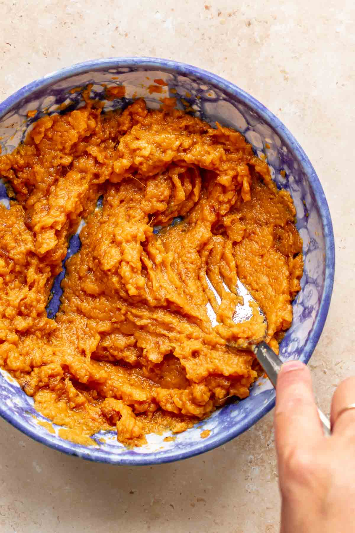 A fork mashes cooked sweet potato in a bowl.