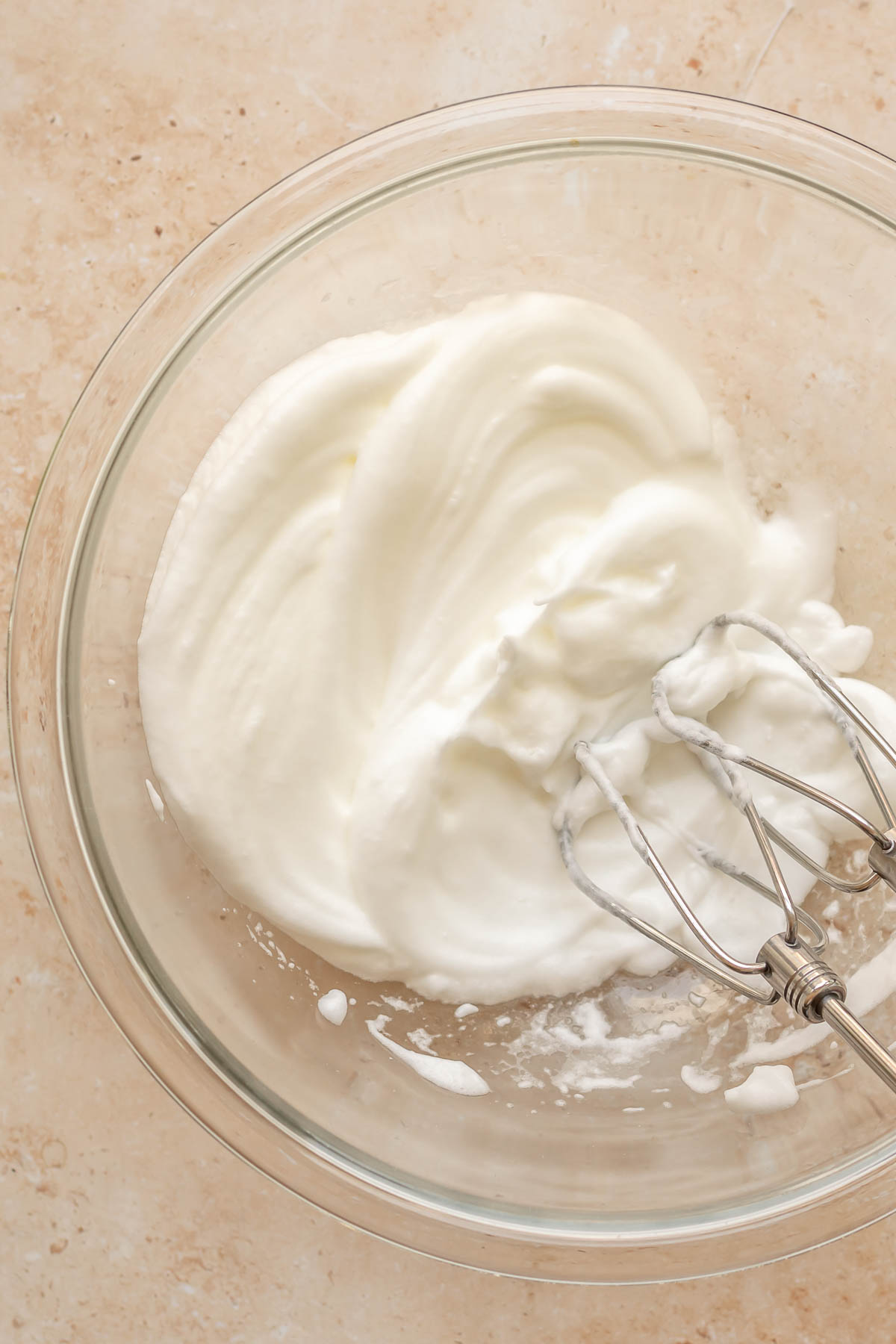 A hand mixes whips egg whites in a bowl.
