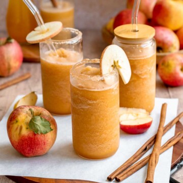 Apple cider slushie poured into glasses with straws and apple garnishes.