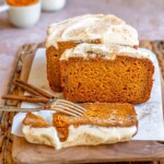 Sliced pumpkin bread with cream cheese frosting on a cutting board.