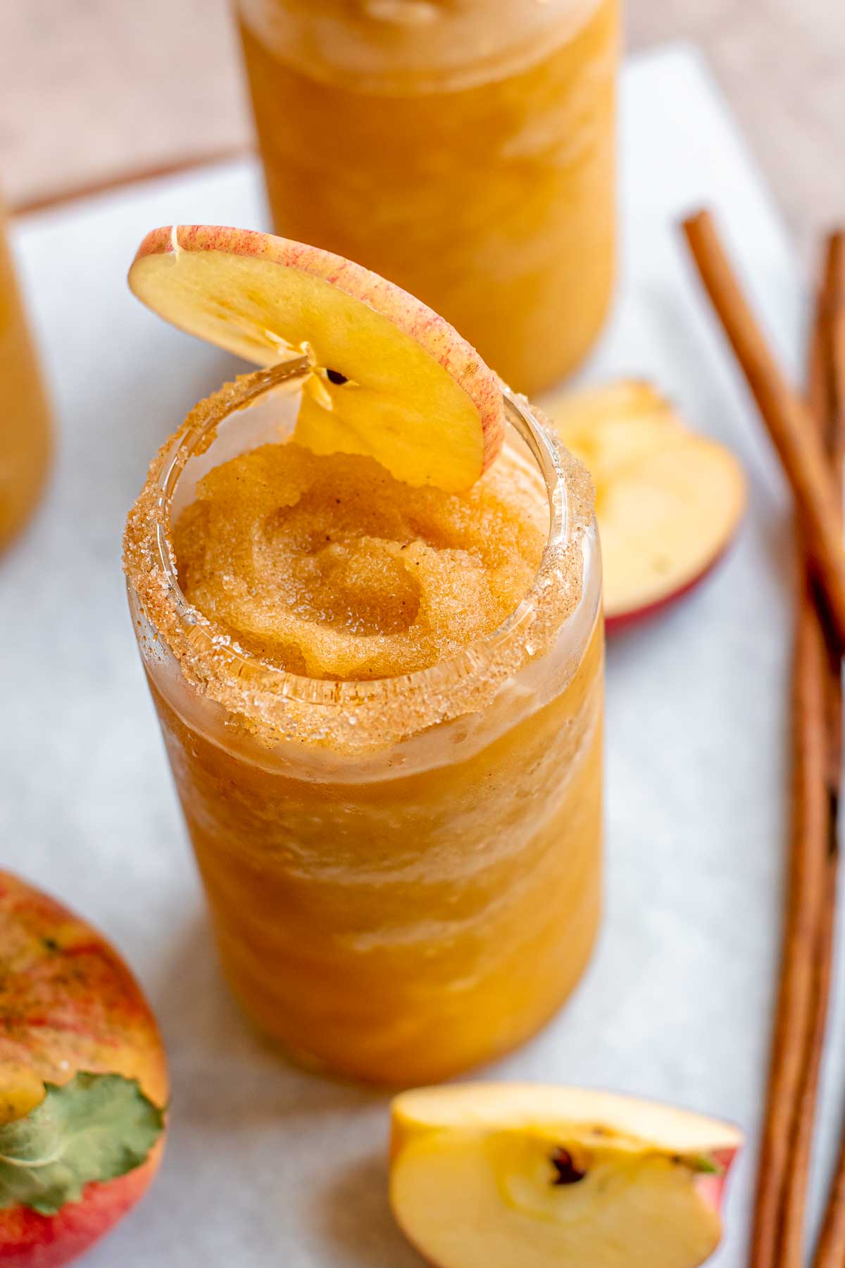 Apple cider slushie in a glass with a slice of apple in the top.