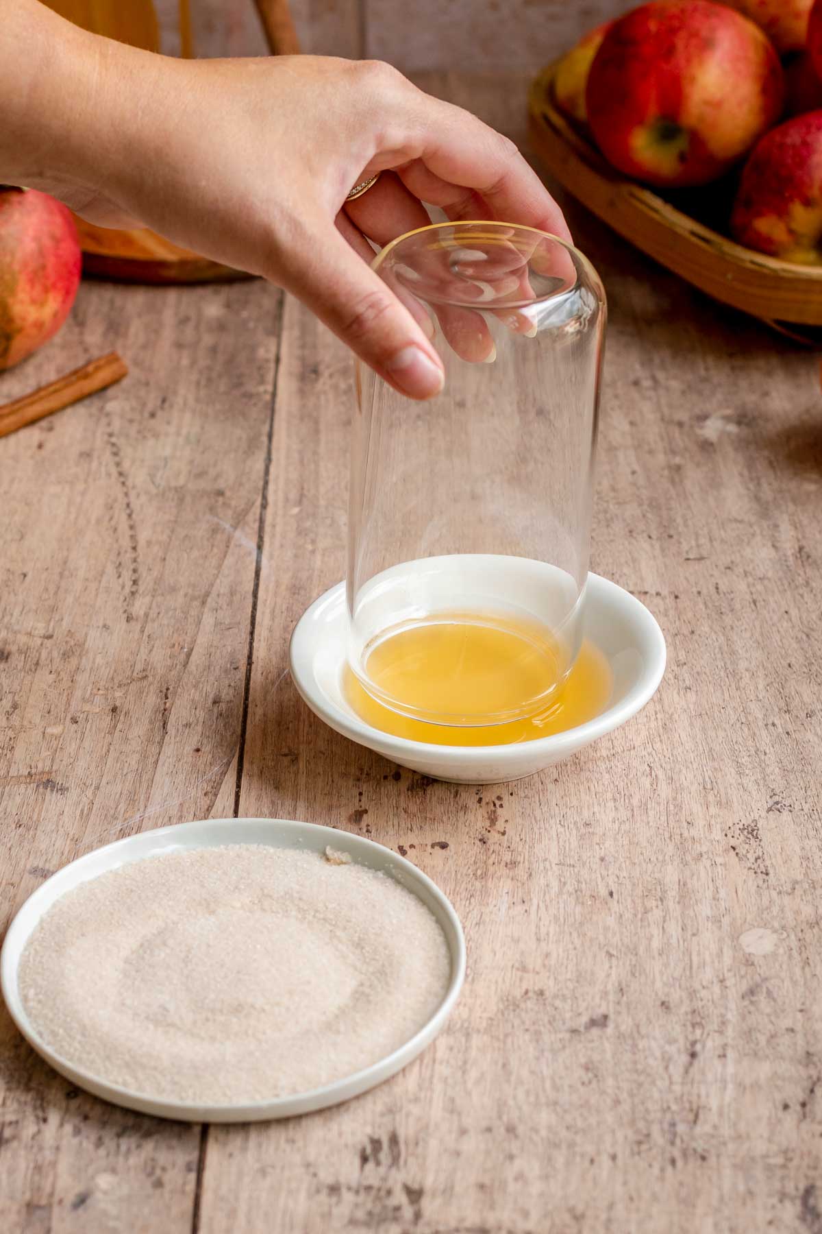 A hand dips the rim of a glass off into apple cider.