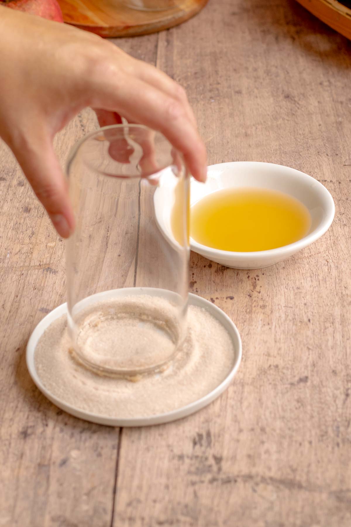 A hand dips the rim of a glass off into cinnamon sugar.