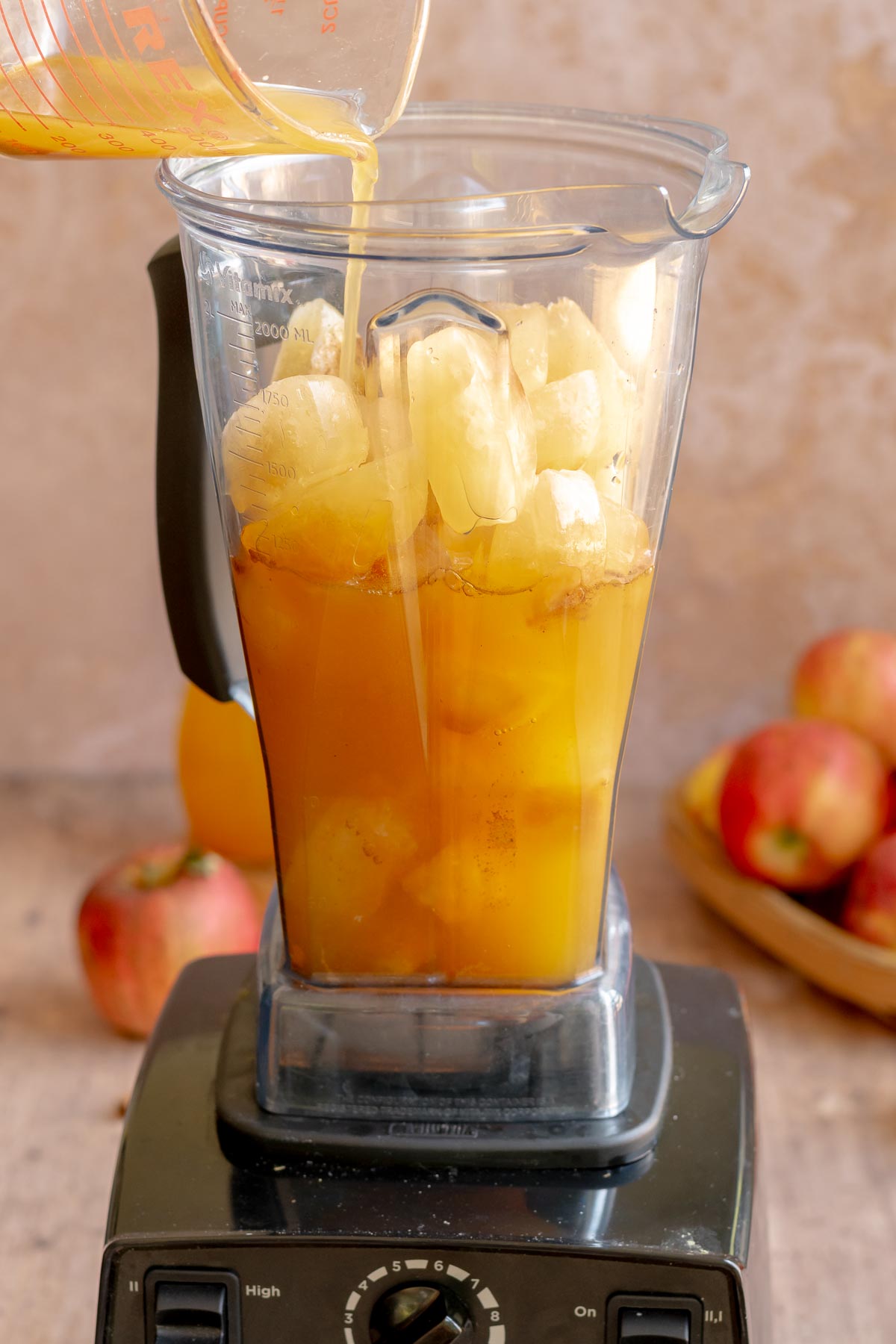 A hand pours apple cider over apple cider ice cubes in a blender.