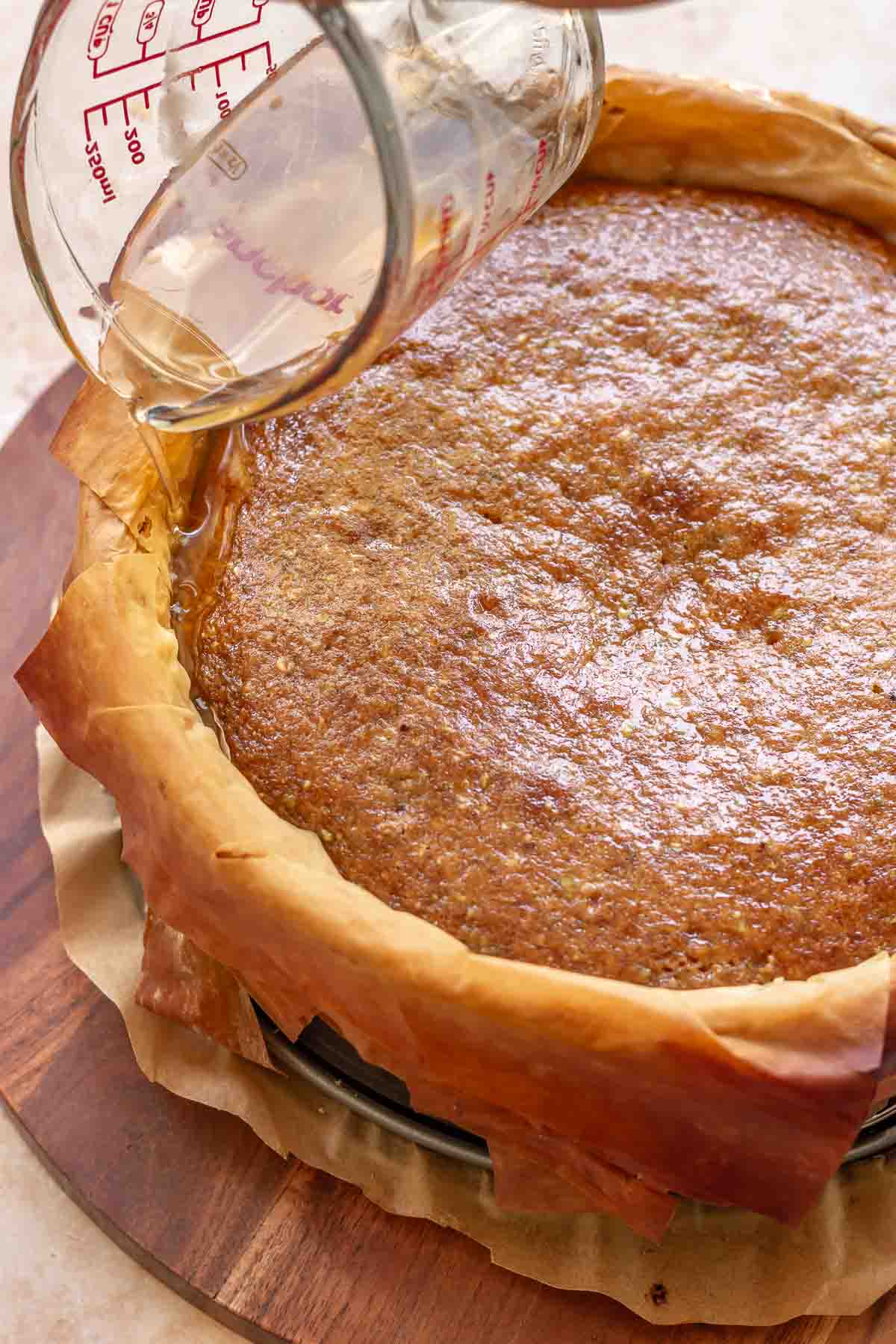 Honey syrup being poured into the sides of the cake.