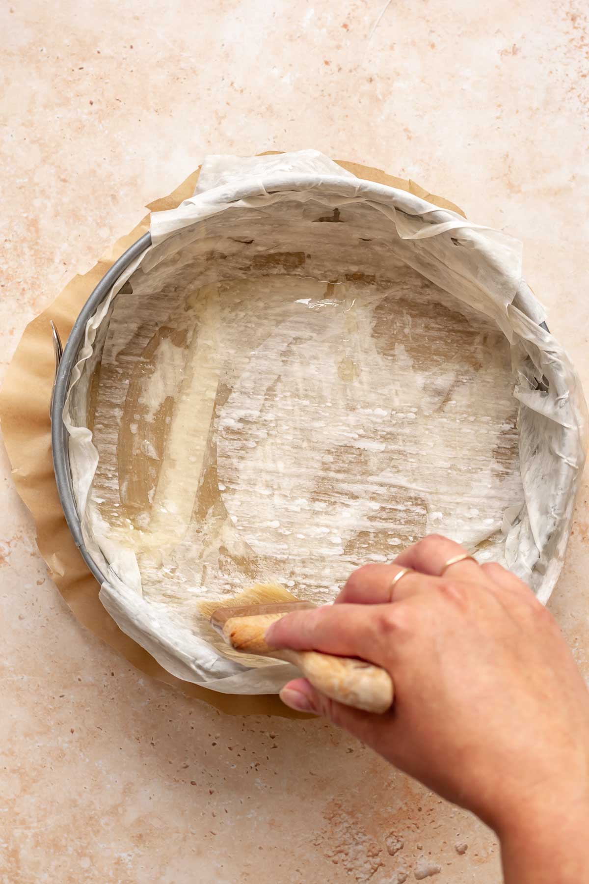 A pastry brush brushes phyllo dough in a pan with butter.