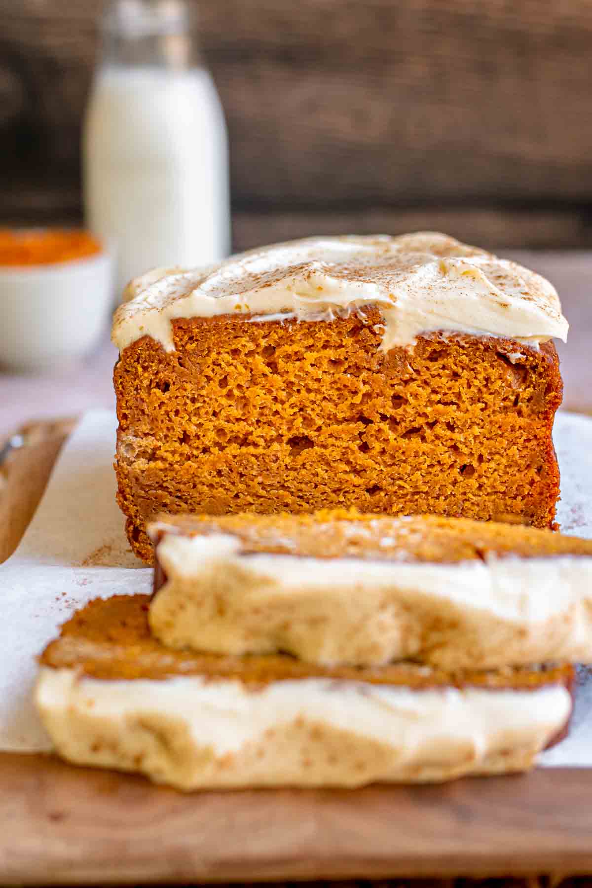 Sliced pumpkin bread with cream cheese frosting on a cutting board.