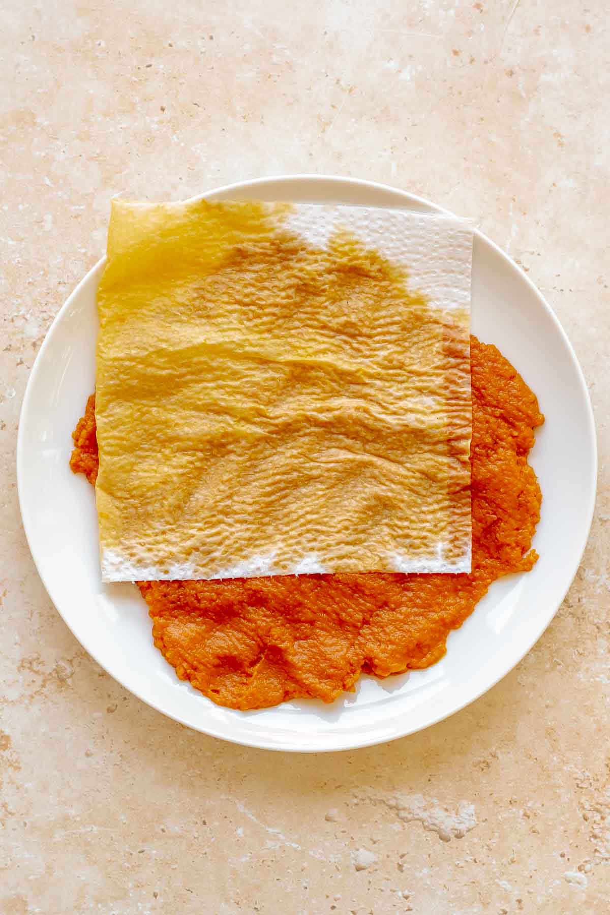 A paper towel presses moisture out of pumpkin puree on a plate.