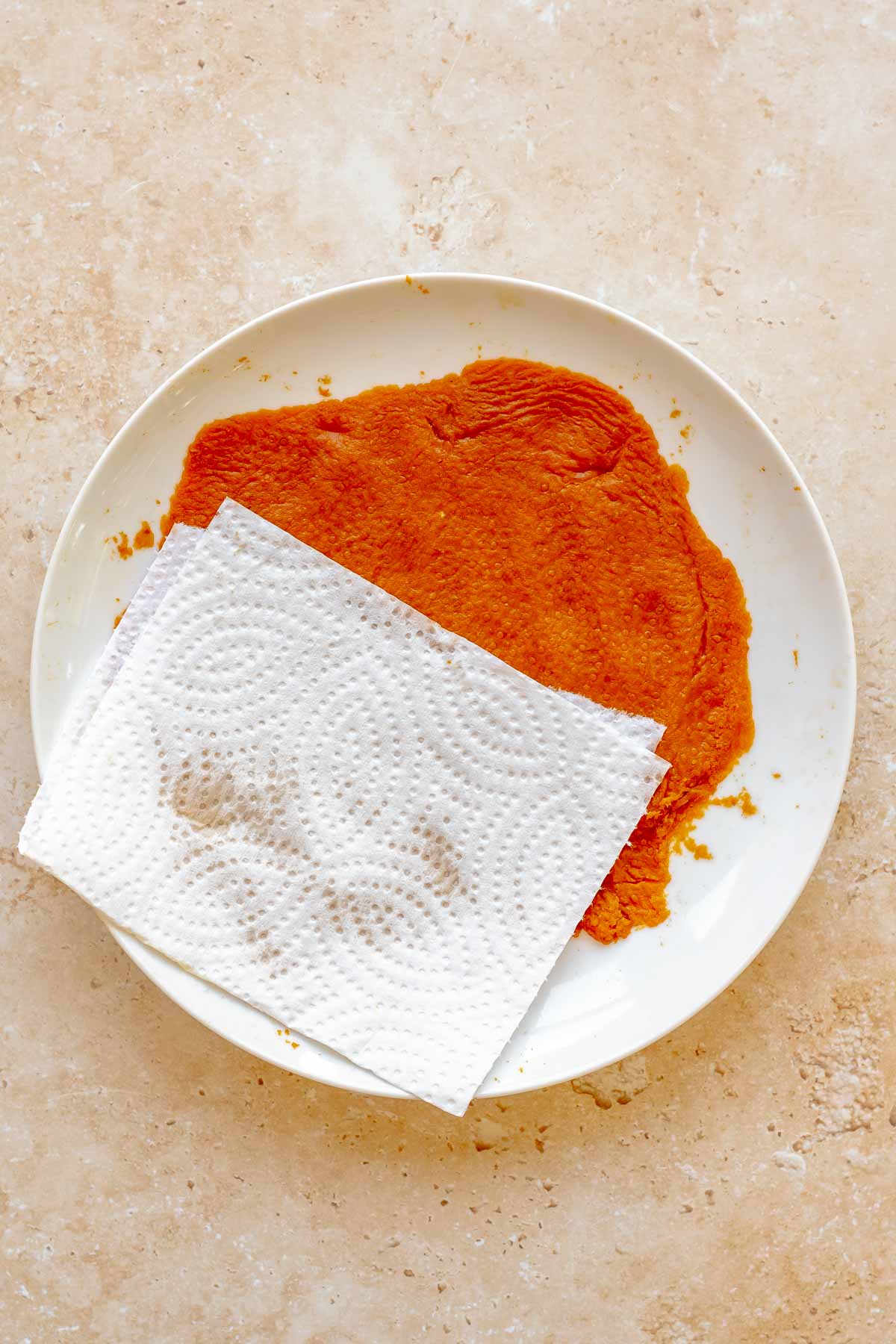 A paper towel is barely saturated from removing water from pumpkin puree on a plate.