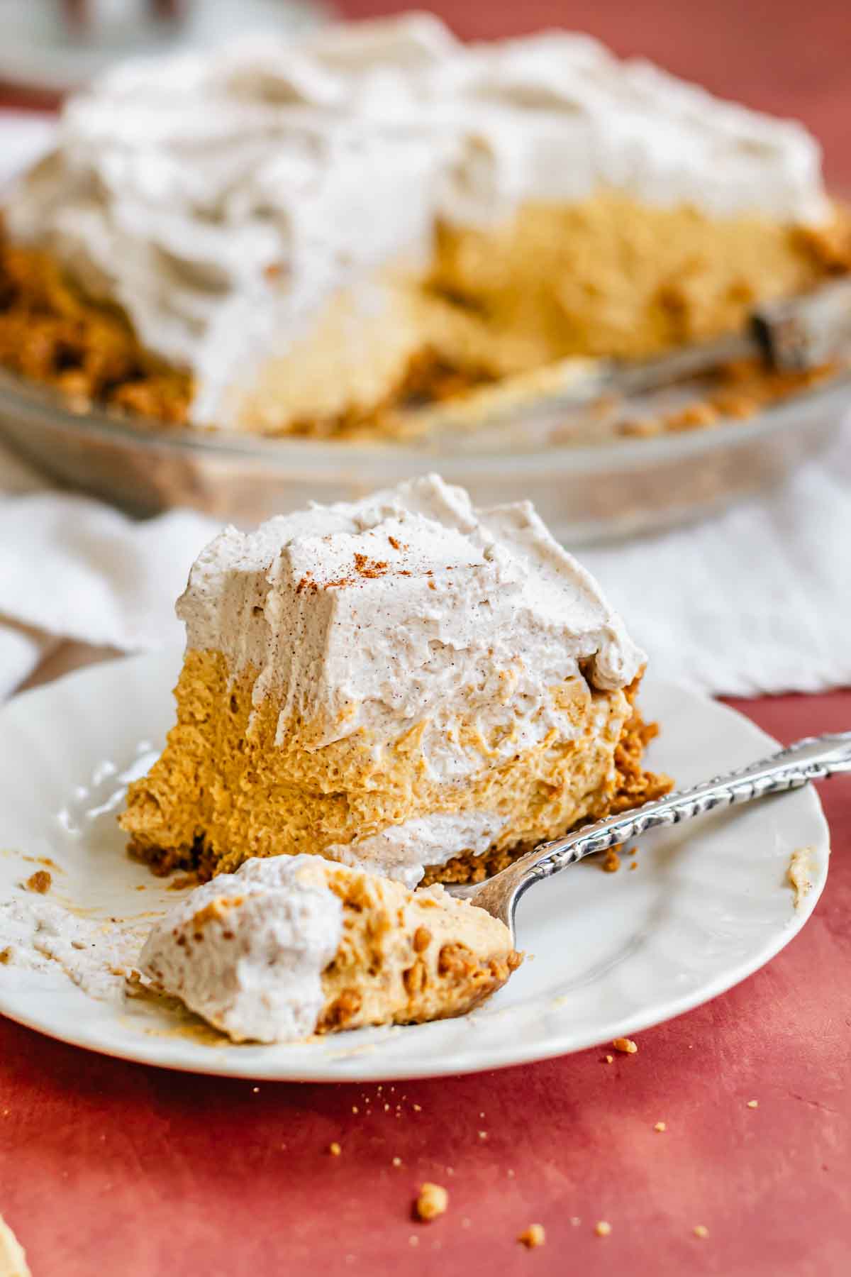 A slice of pumpkin mousse pie on a plate. A fork holds a bite.