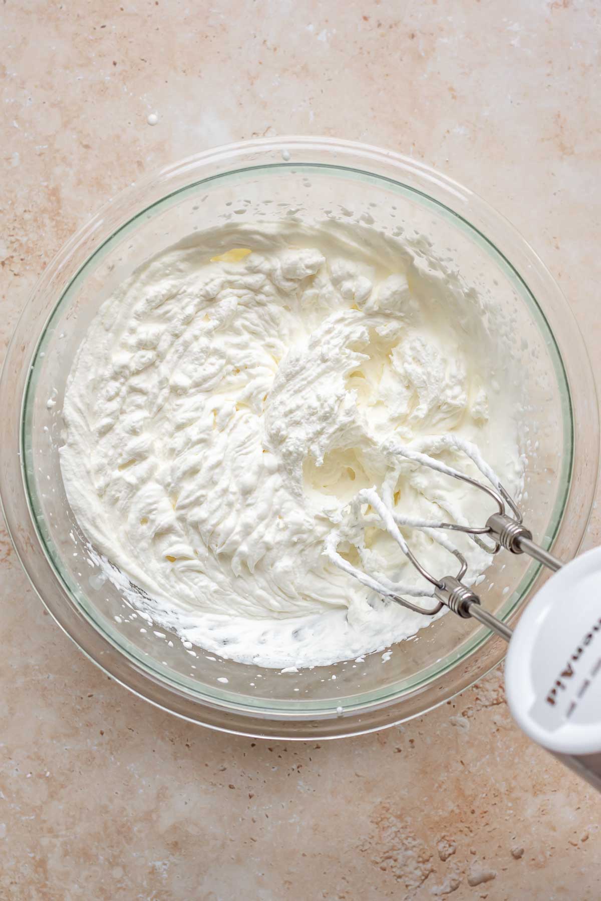 A hand mixer mixes whipped cream in a bowl.
