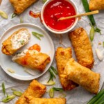 Crab rangoon egg rolls on a platter with dipping sauce.