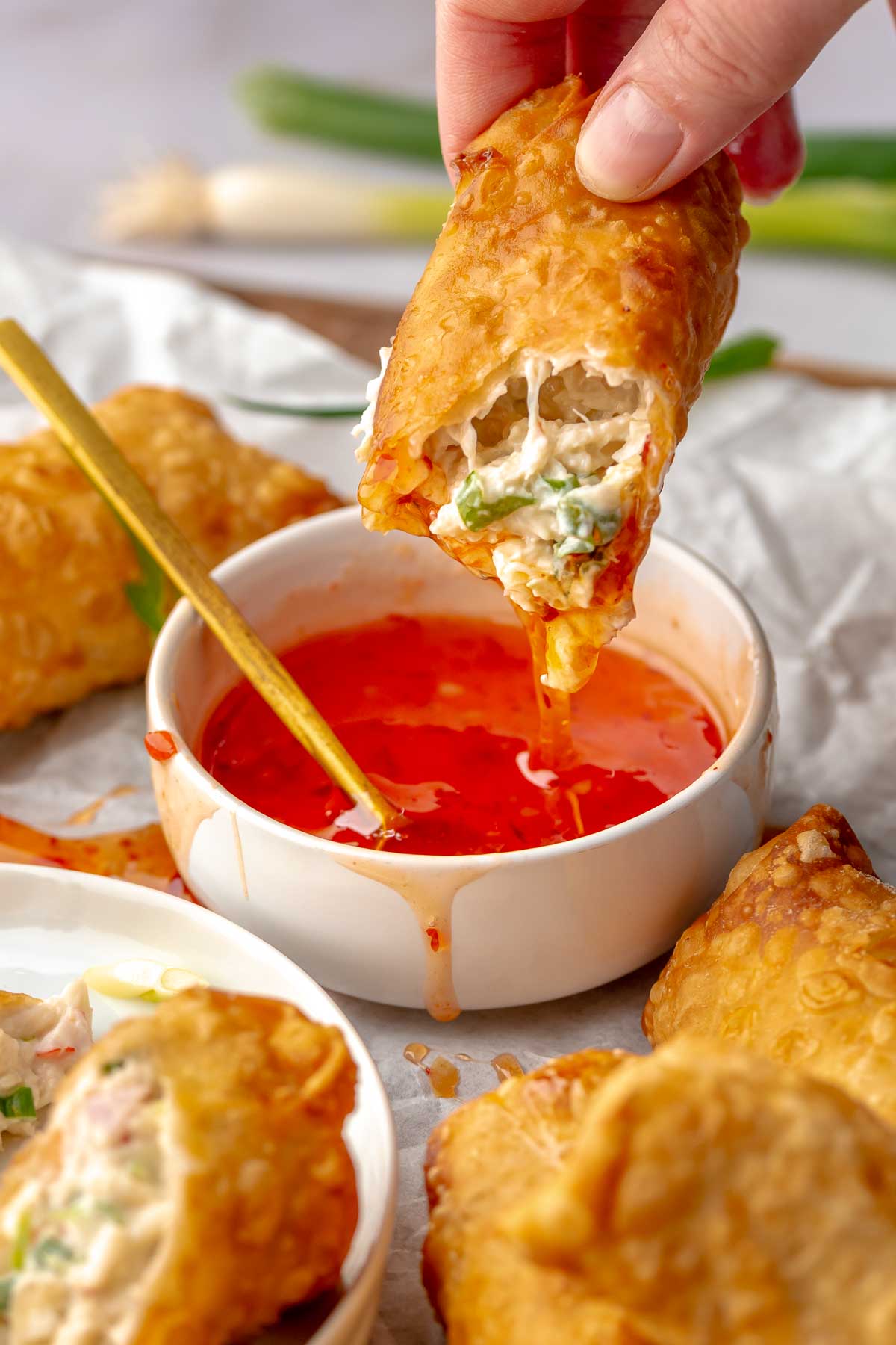 Crab rangoon egg roll being dipped into sweet chili sauce.