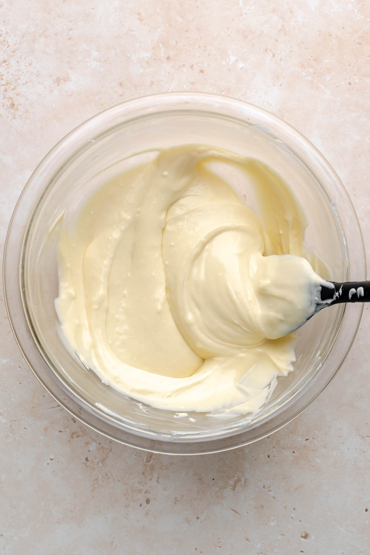A rubber spatula smooths out cream cheese in a bowl.