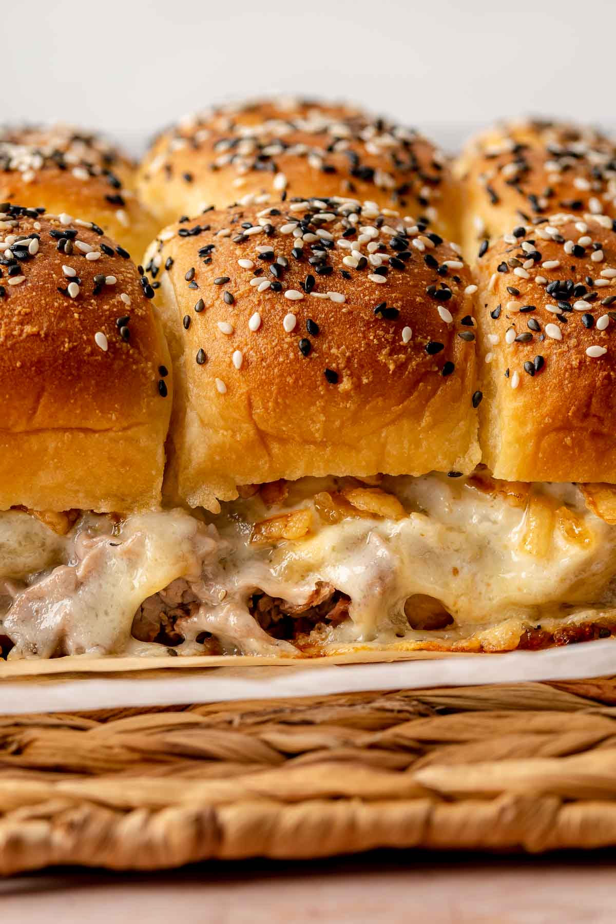 Baked beef sliders with cheese melting out the sides.