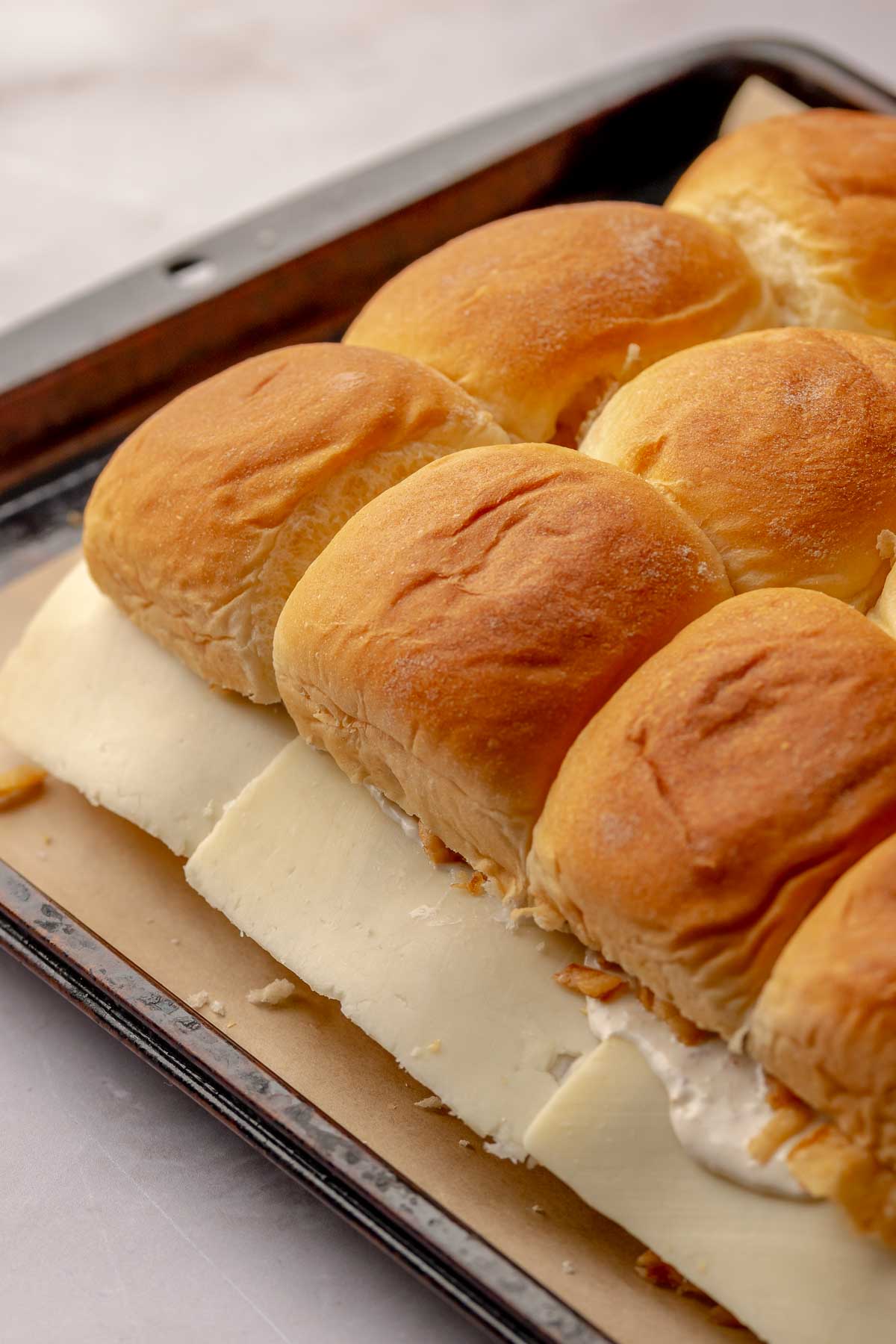 Sliders fully assembled on a pan. Cheese hangs over the sides of the buns.