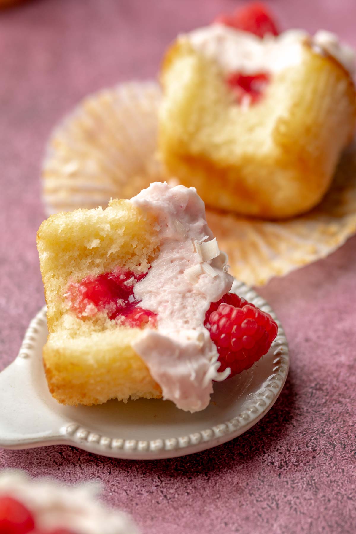 Raspberry cupcake laying on the side with a bite removed.