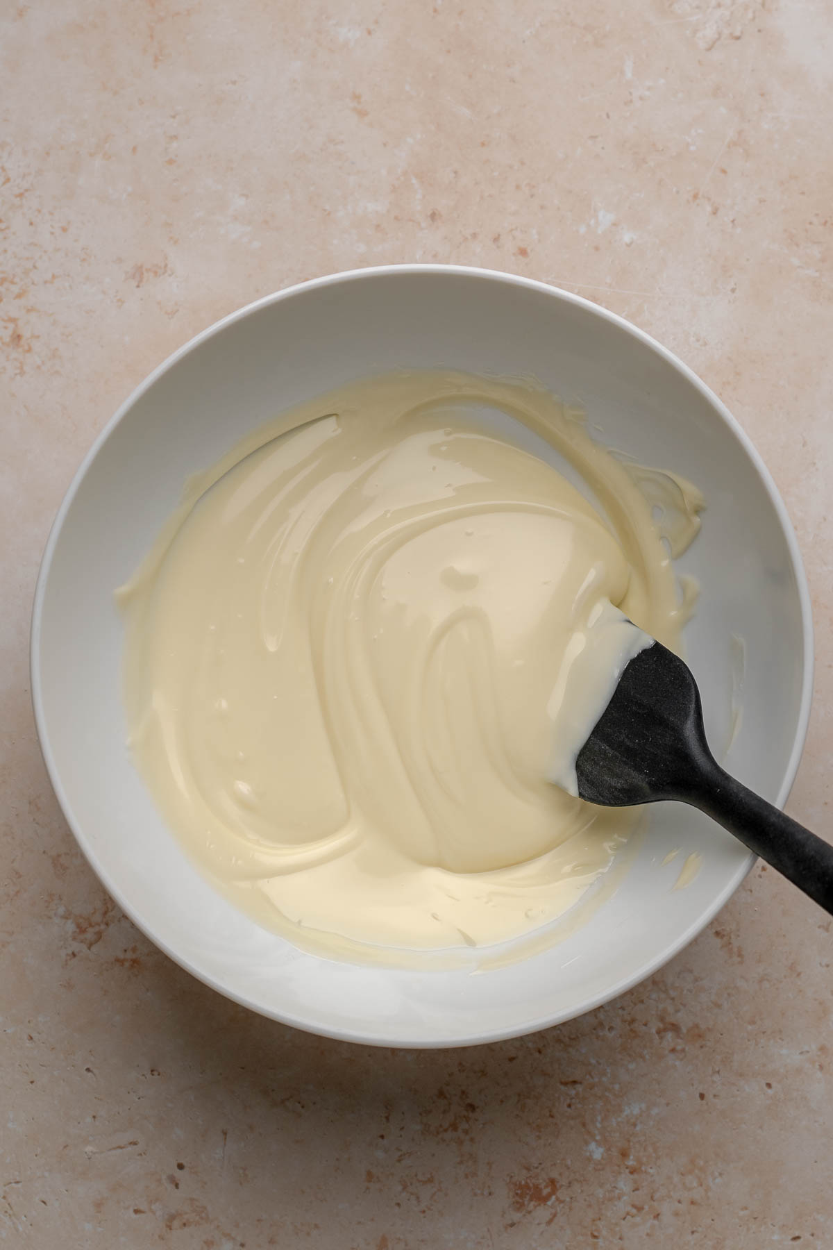 Melted white chocolate in a bowl with a spatula.