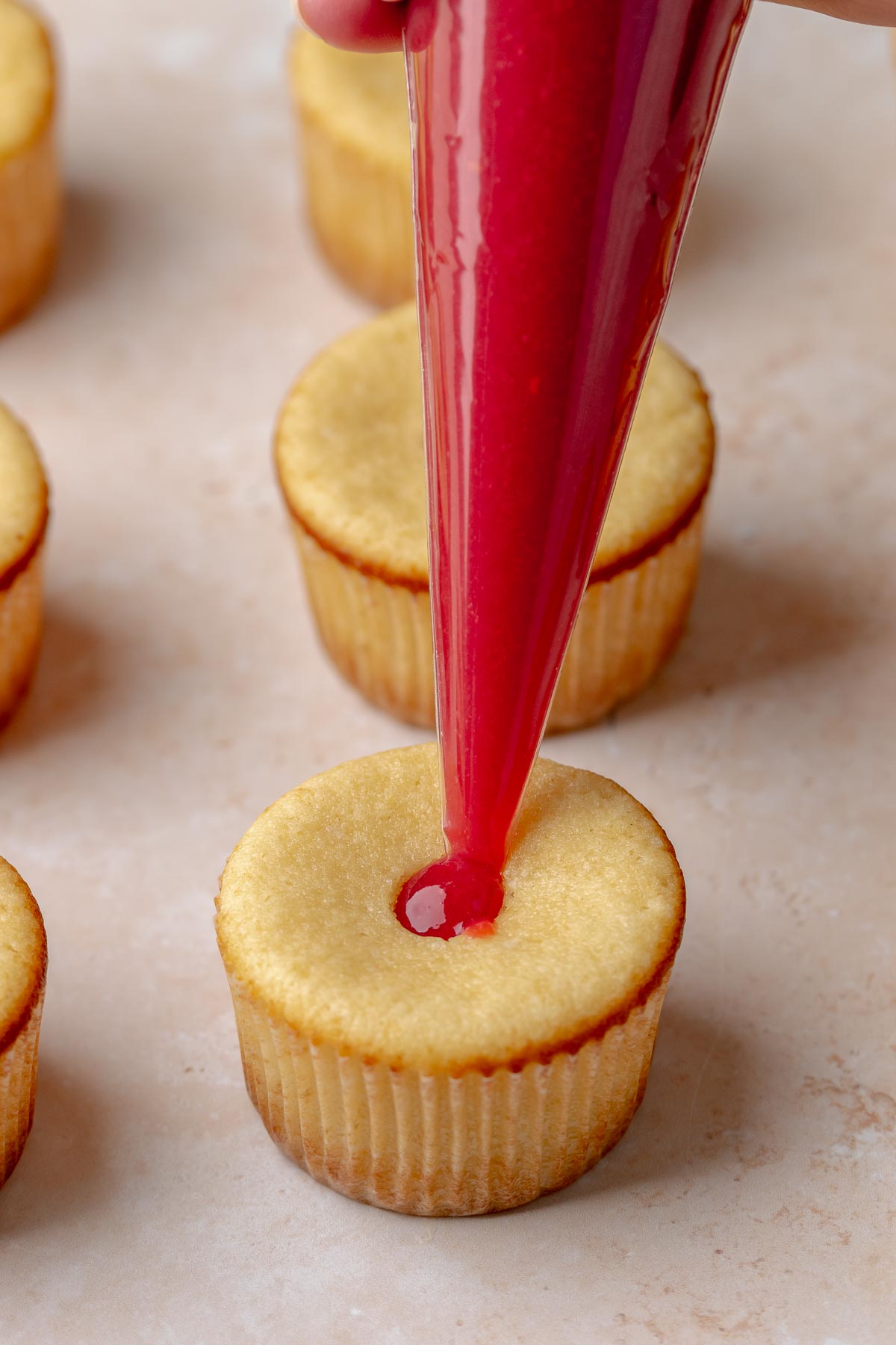 A piping bag adds raspberry filling into a cupcakes.