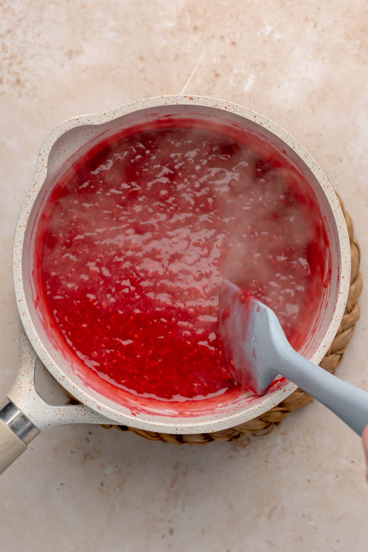 A spatula mixes hot raspberry puree in a pot.