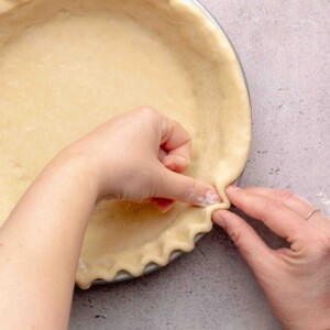 Two hands crimping edges of pie dough.