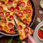 A hand pulls a piece of pizza from a cast iron skillet.