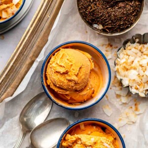 Thai tea ice cream in bowls with coconut and tea next to it.