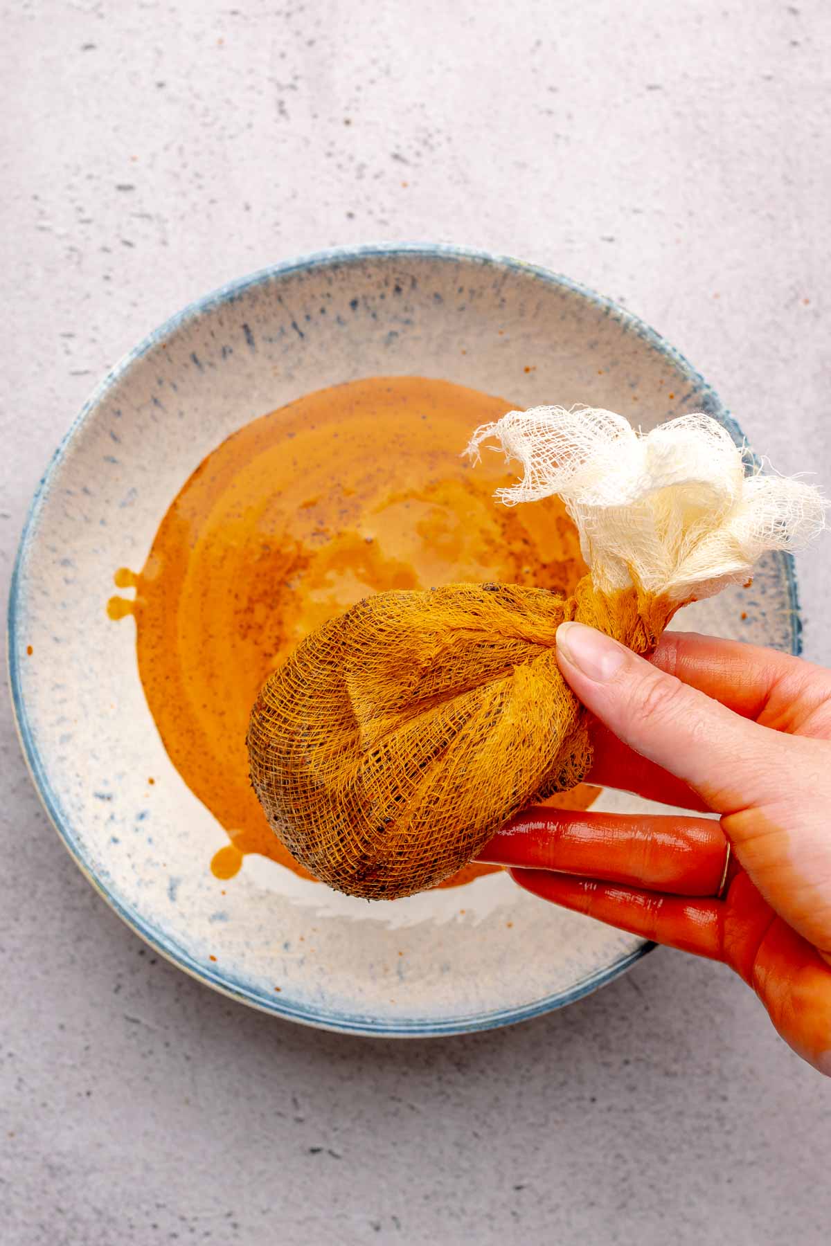 A hand squeezes Thai tea out of a cheesecloth.