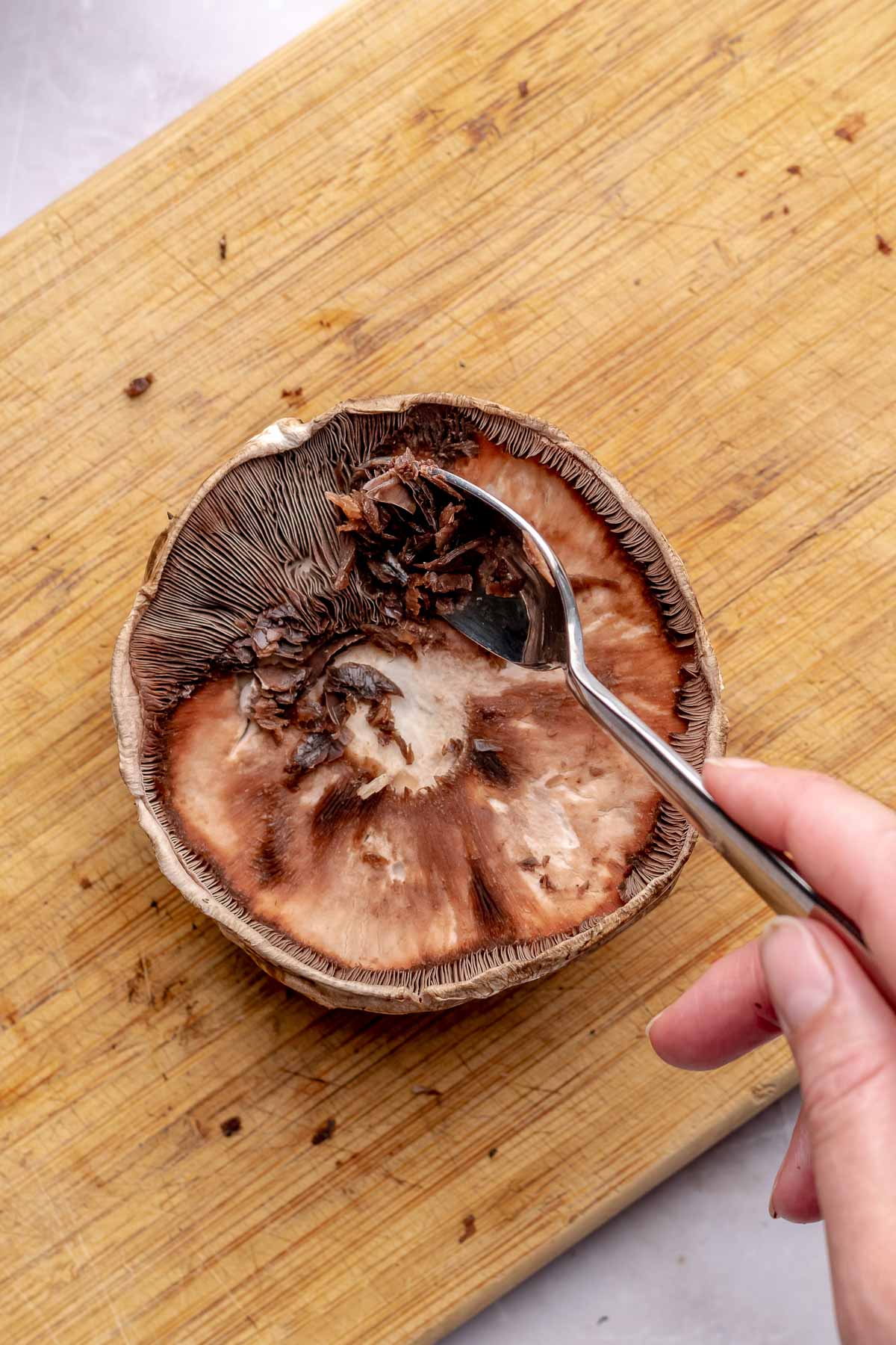 A spoon cleans out gills from a portobello mushroom.