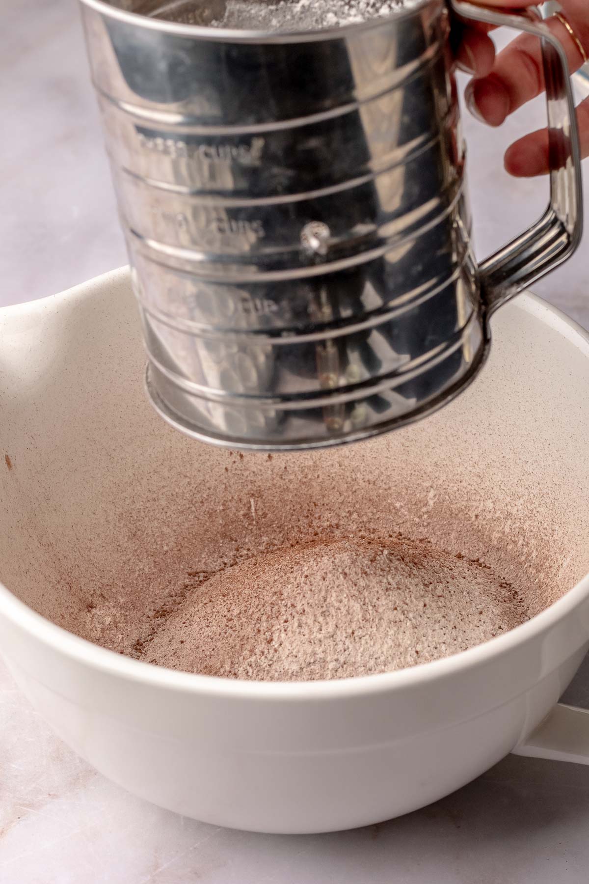 A sifter sifts flour and cocoa into a bowl