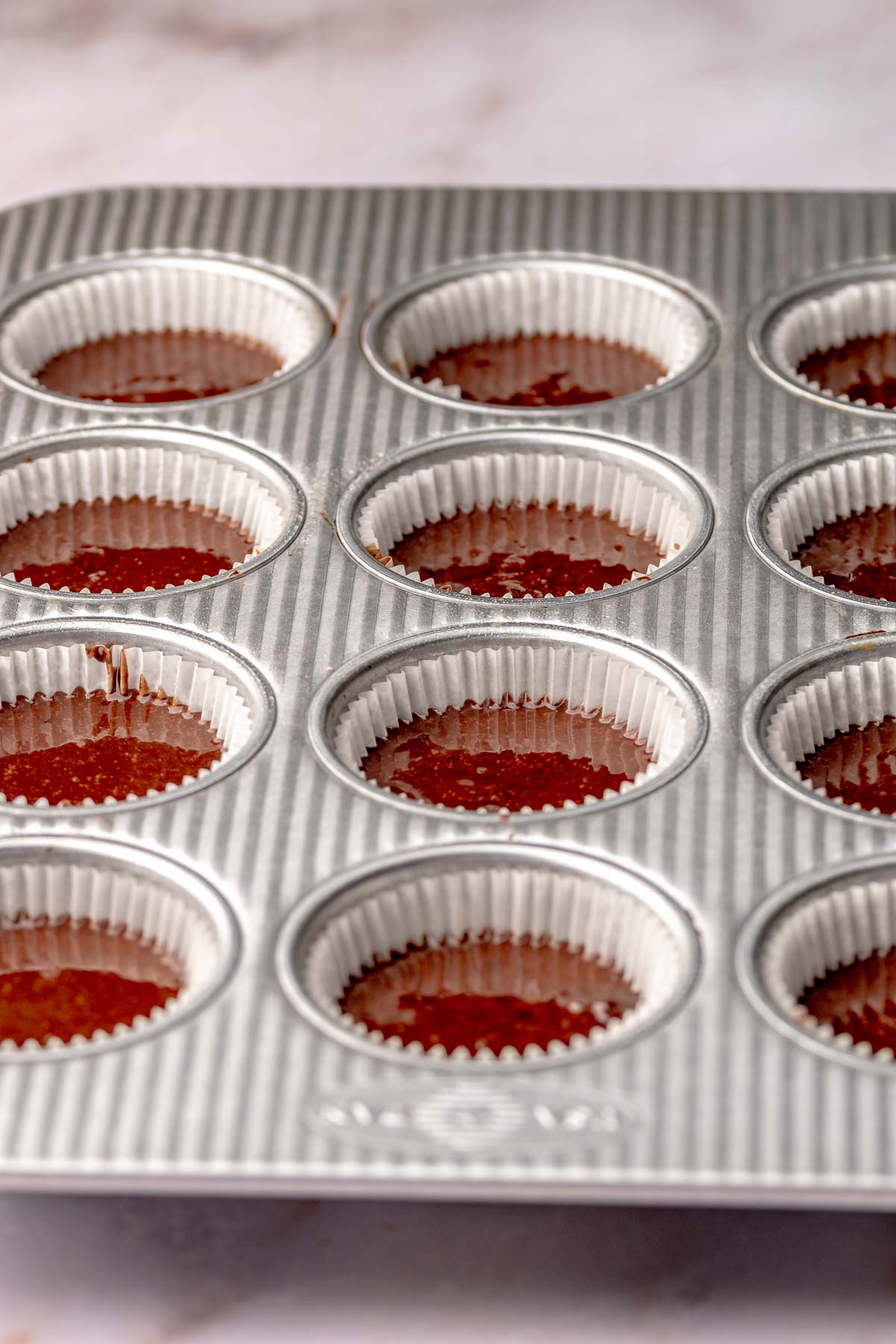 Filled, pre-baked chocolate cupcakes in a muffin tin.
