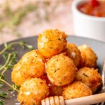 A pile of fried goat cheese balls on a plate with honey on top.