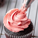 A piping bag pipes strawberry swiss meringue buttercream o a cupcake.