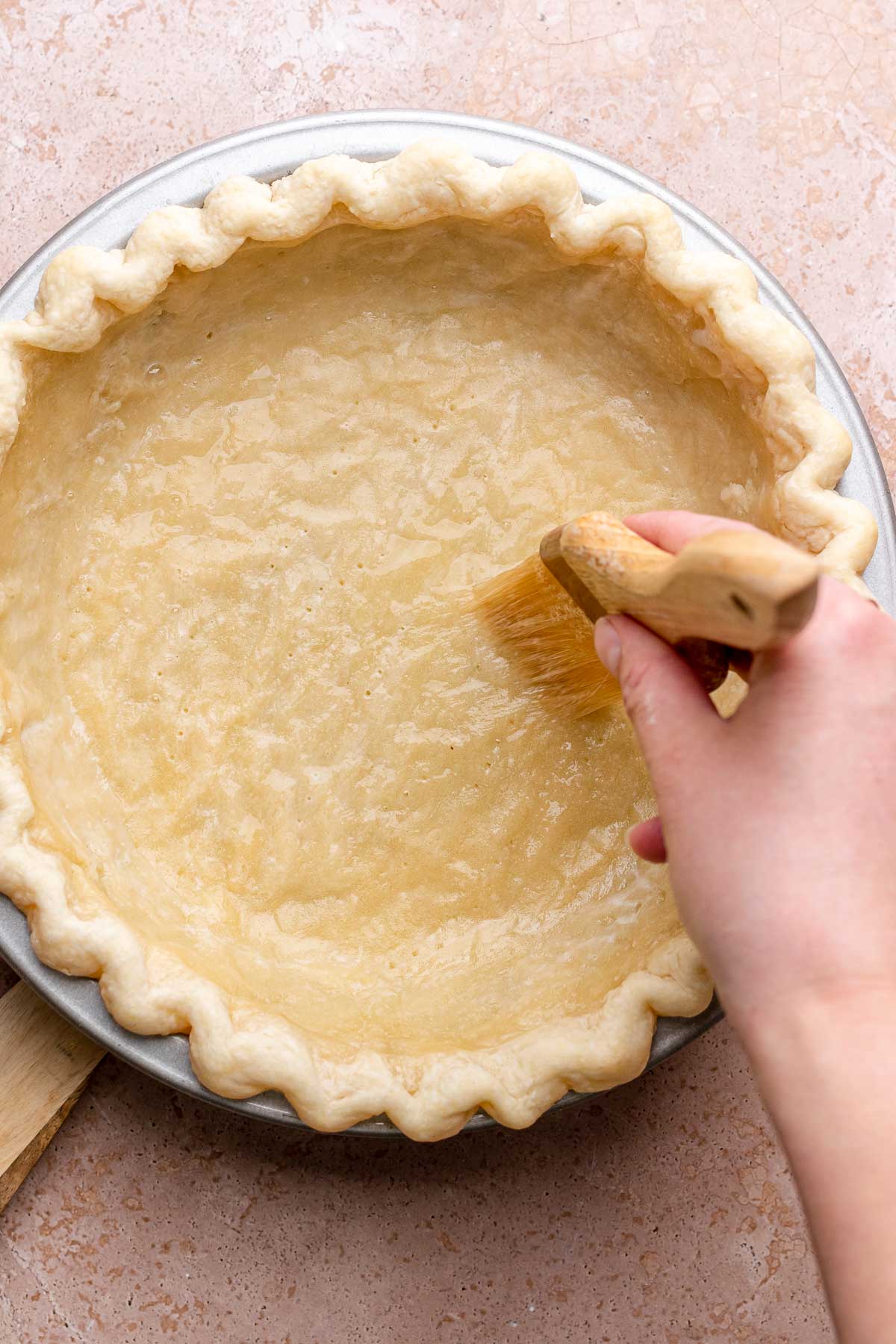 A pastry brush swipes egg whites onto a pie crust.