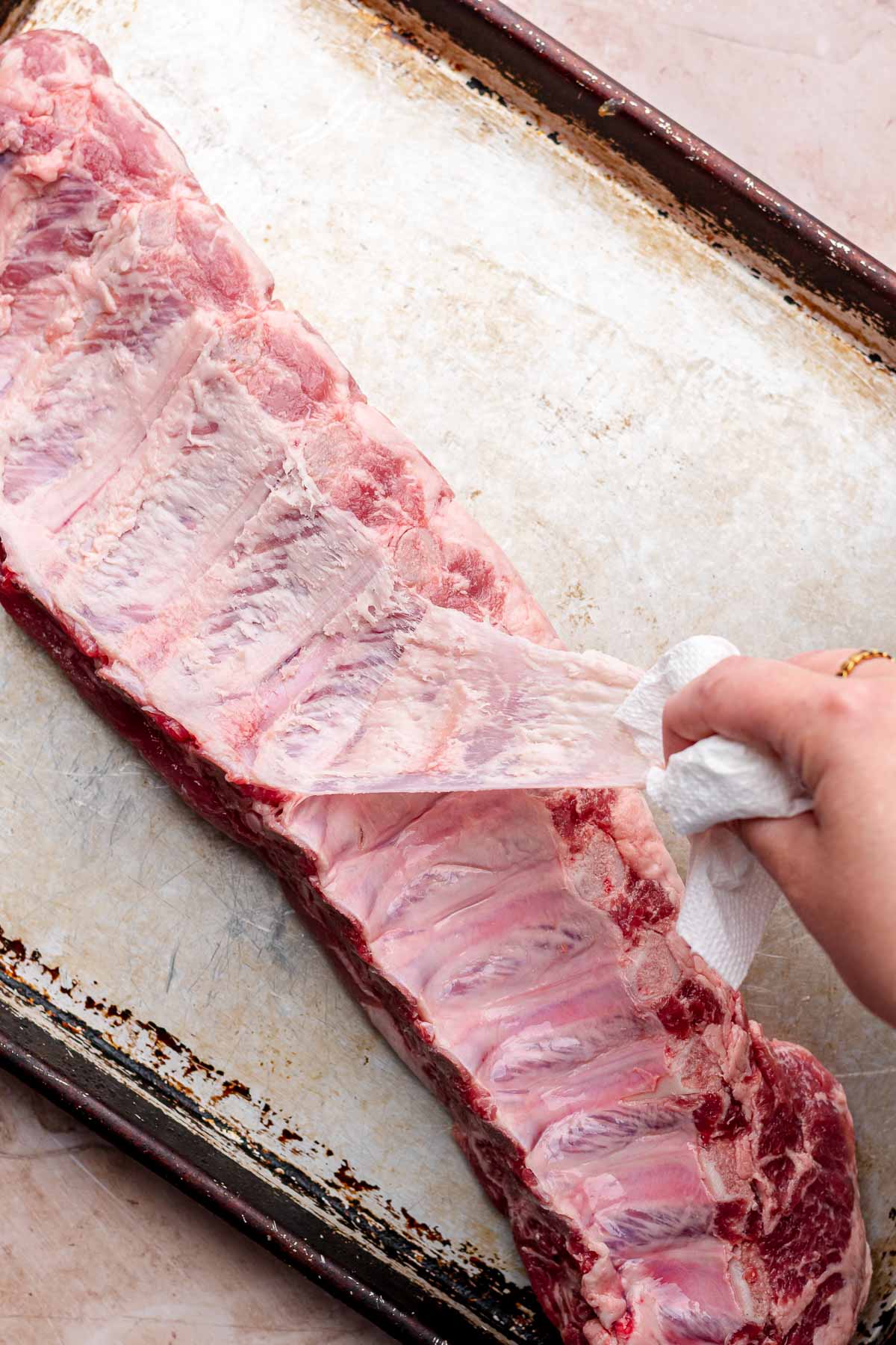 A hand holding a paper towel pulls off silver skin from the ribs.