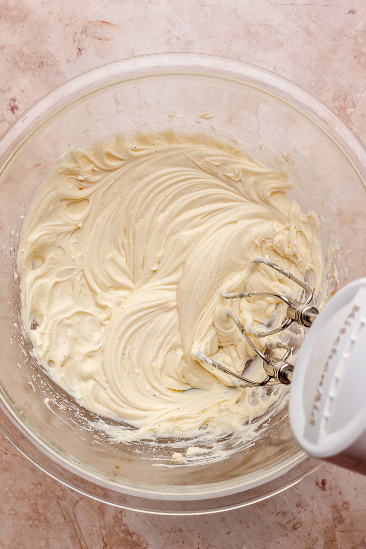 A hand mixer mixes honey mascarpone frosting in a bowl.