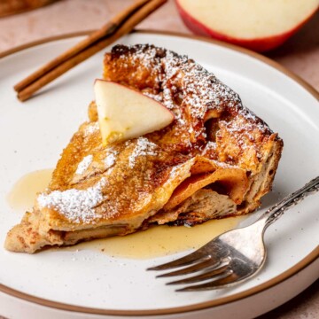 A slice of cinnamon apple dutch baby on a plate with a fork next to it.