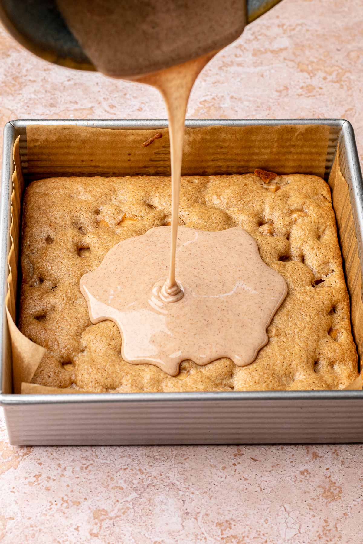 Cinnamon icing being drizzled onto baked cinnamon apple blondies in a pan.