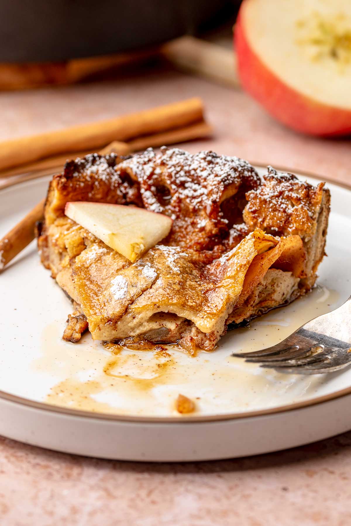 A slice of cinnamon apple dutch baby on a plate with a fork next to it. The tip bite is removed.