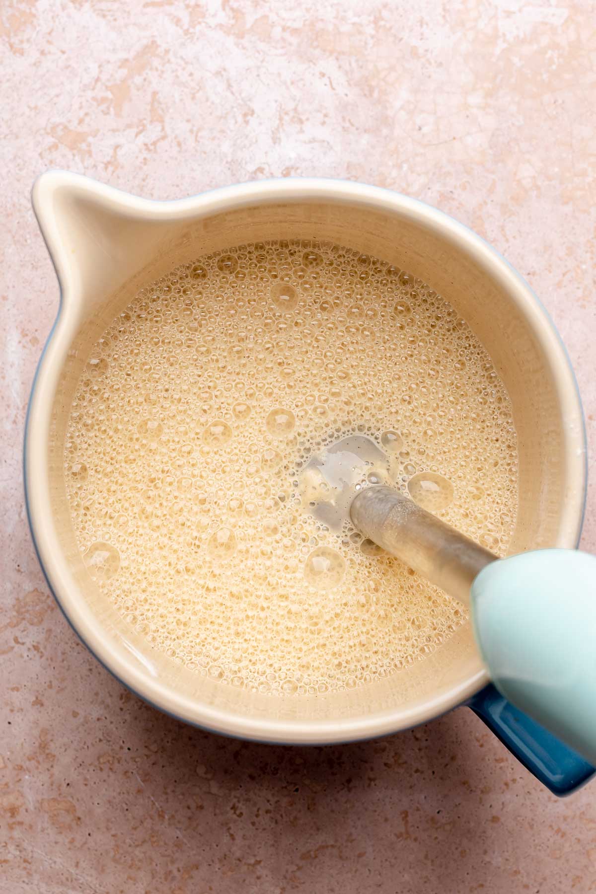 An immersion blender blends the batter in a bowl.
