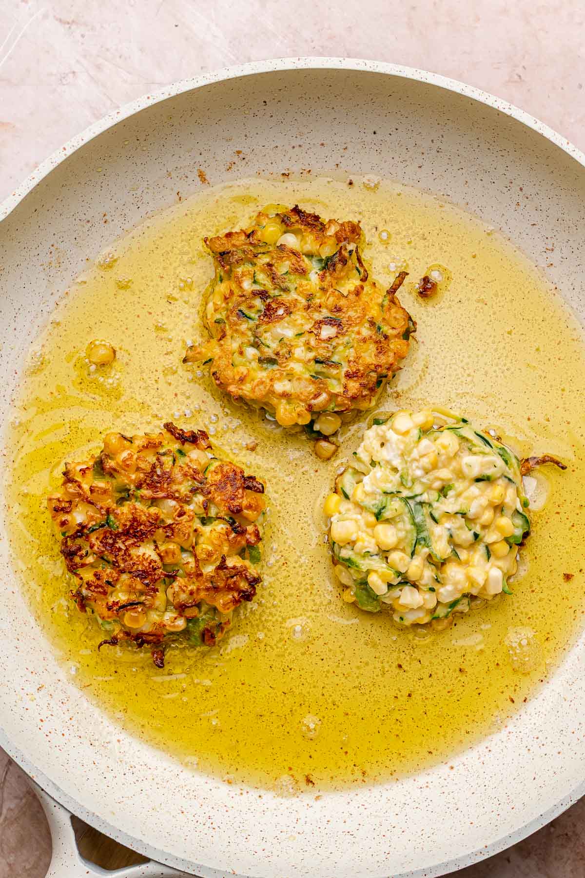 Corn and zucchini fritters frying in a pan.