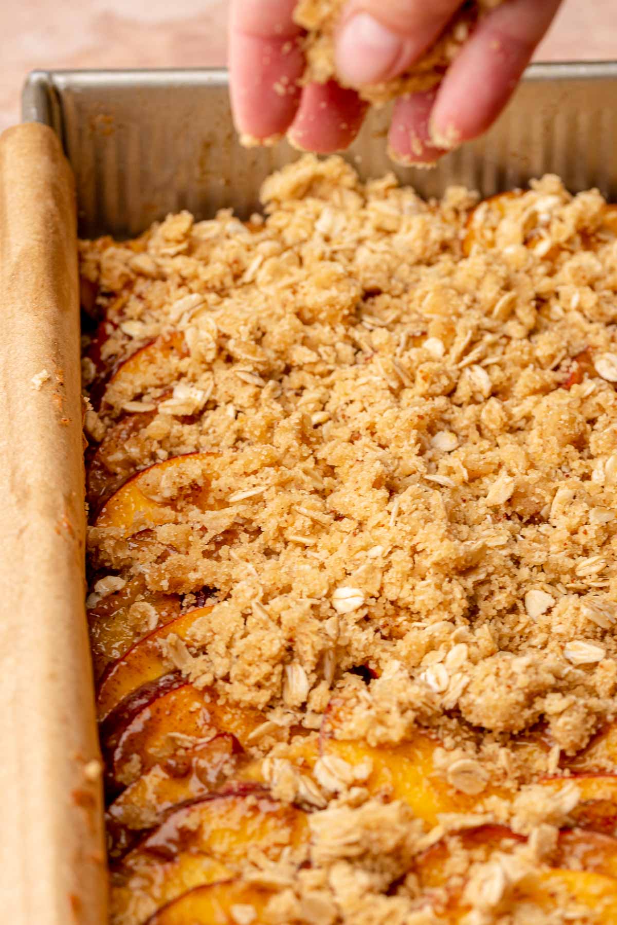 A hand adds oatmeal crumble onto peach bars.